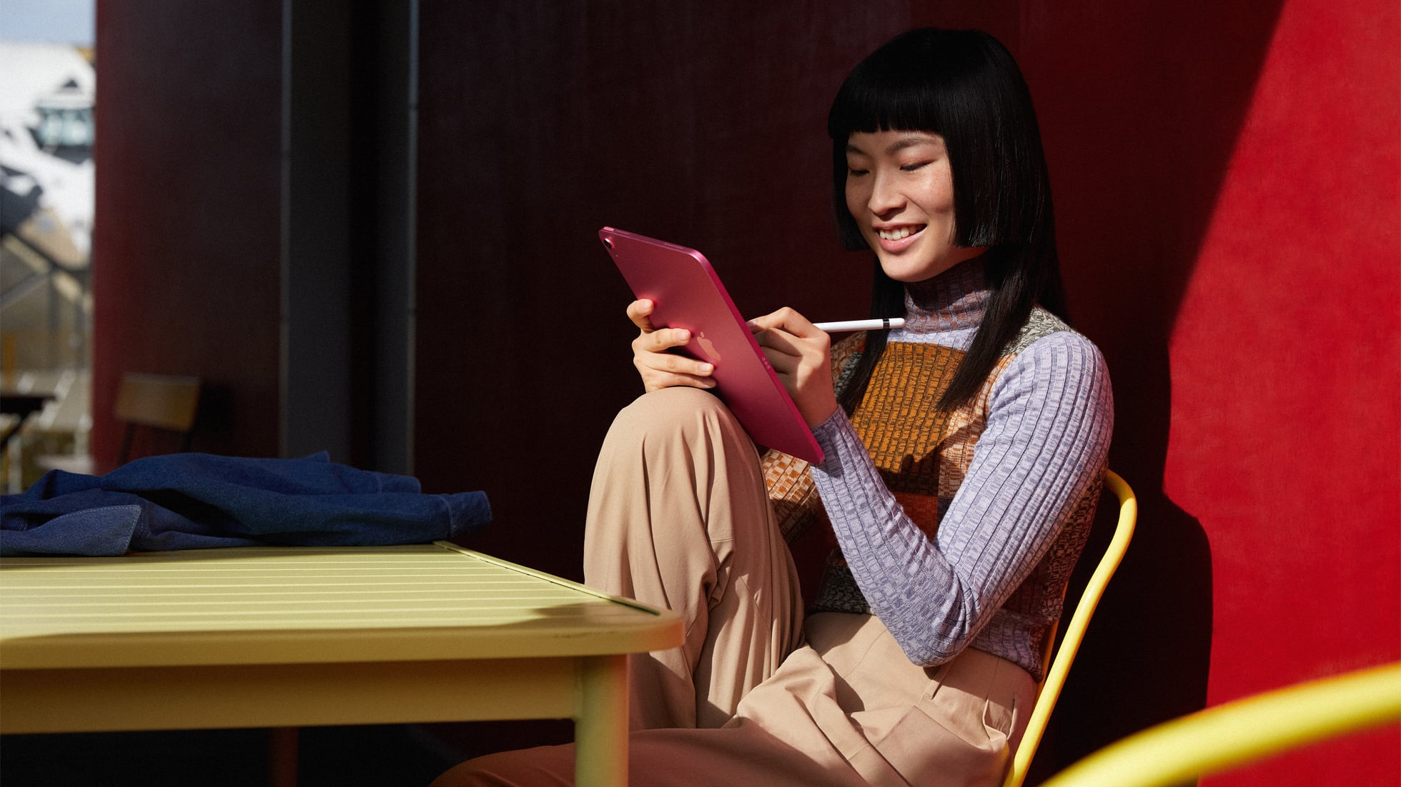 A young woman holding a tenth-generation iPad in one hand and using an Apple Pencil in the other is depicted in this lifestyle image from Apple