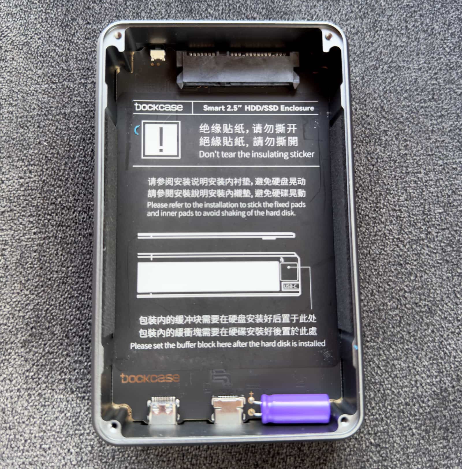 A top-down view of the DockCase external storage enclosure with the metal cover removed, exposing an insulating sticker, SATA III interface and capacitor on the inside
