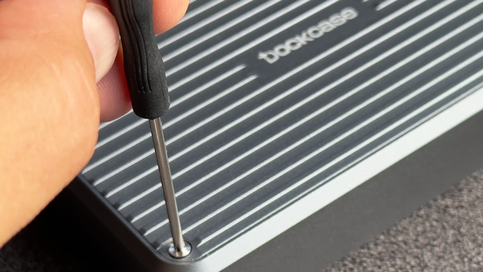 Closeup showing a male hand holding a screwdriver, tightening a Phillips Head #00 screw in a corner of the DockCase external storage enclosure.