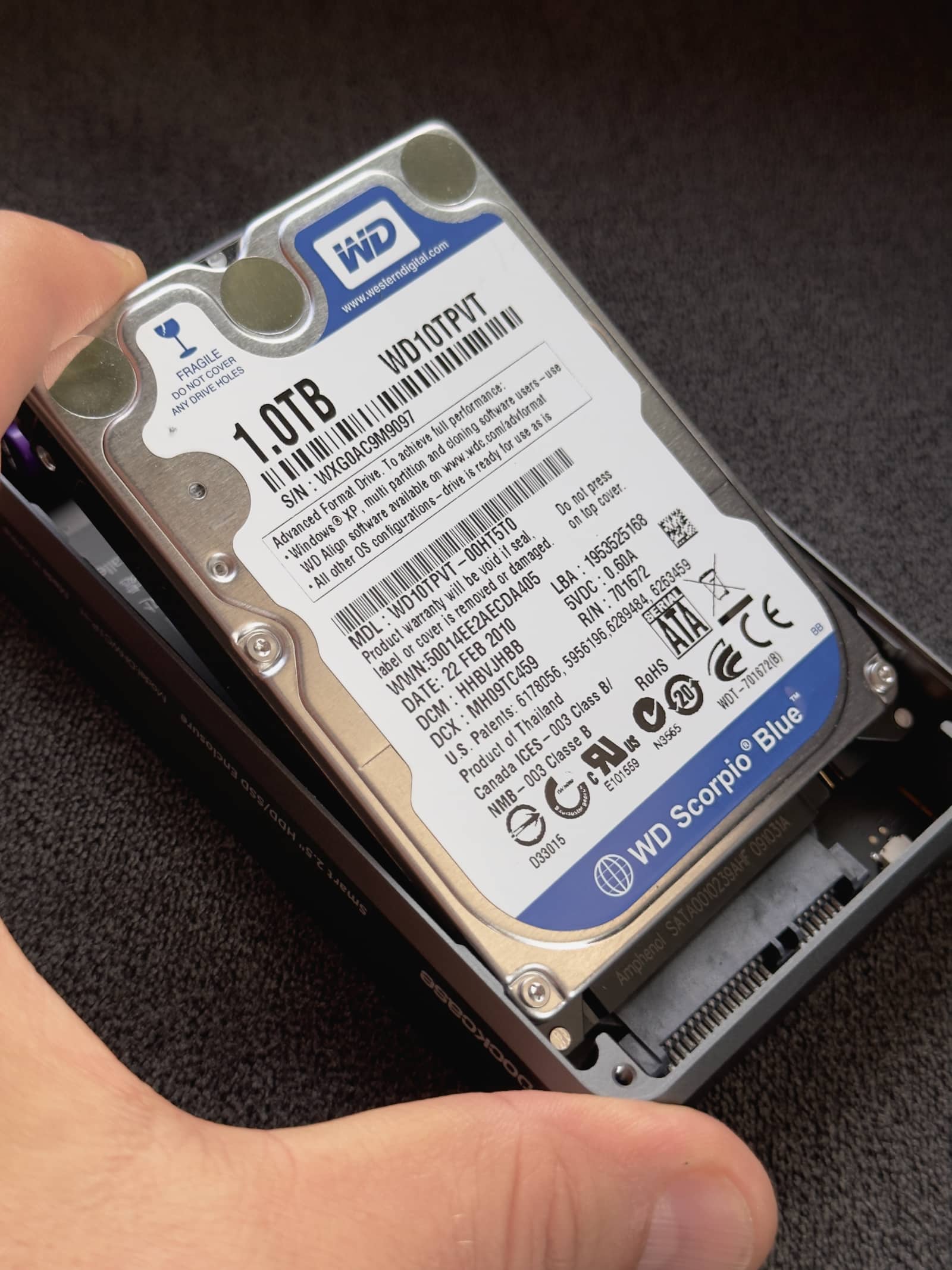 Closeup showing a male hand installing a 2.5-inch Western Digital hard drive into a DockCase external storage enclosure, connecting the drive to the SATA interface 