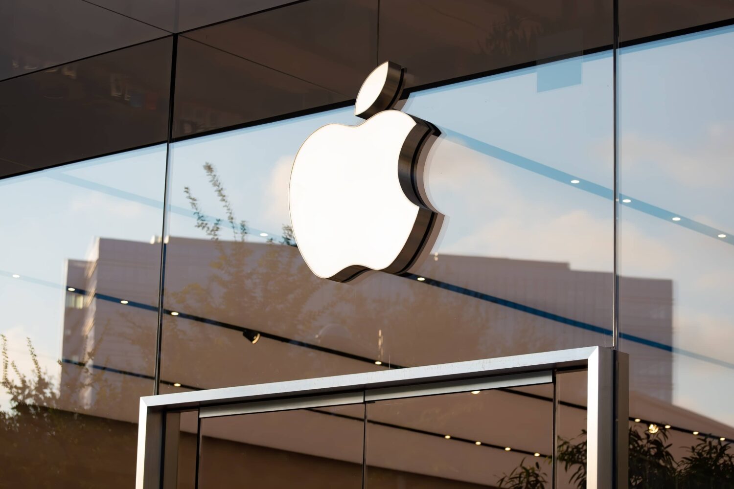 Closeup of an Apple logo above entrance to a glass Apple retail store