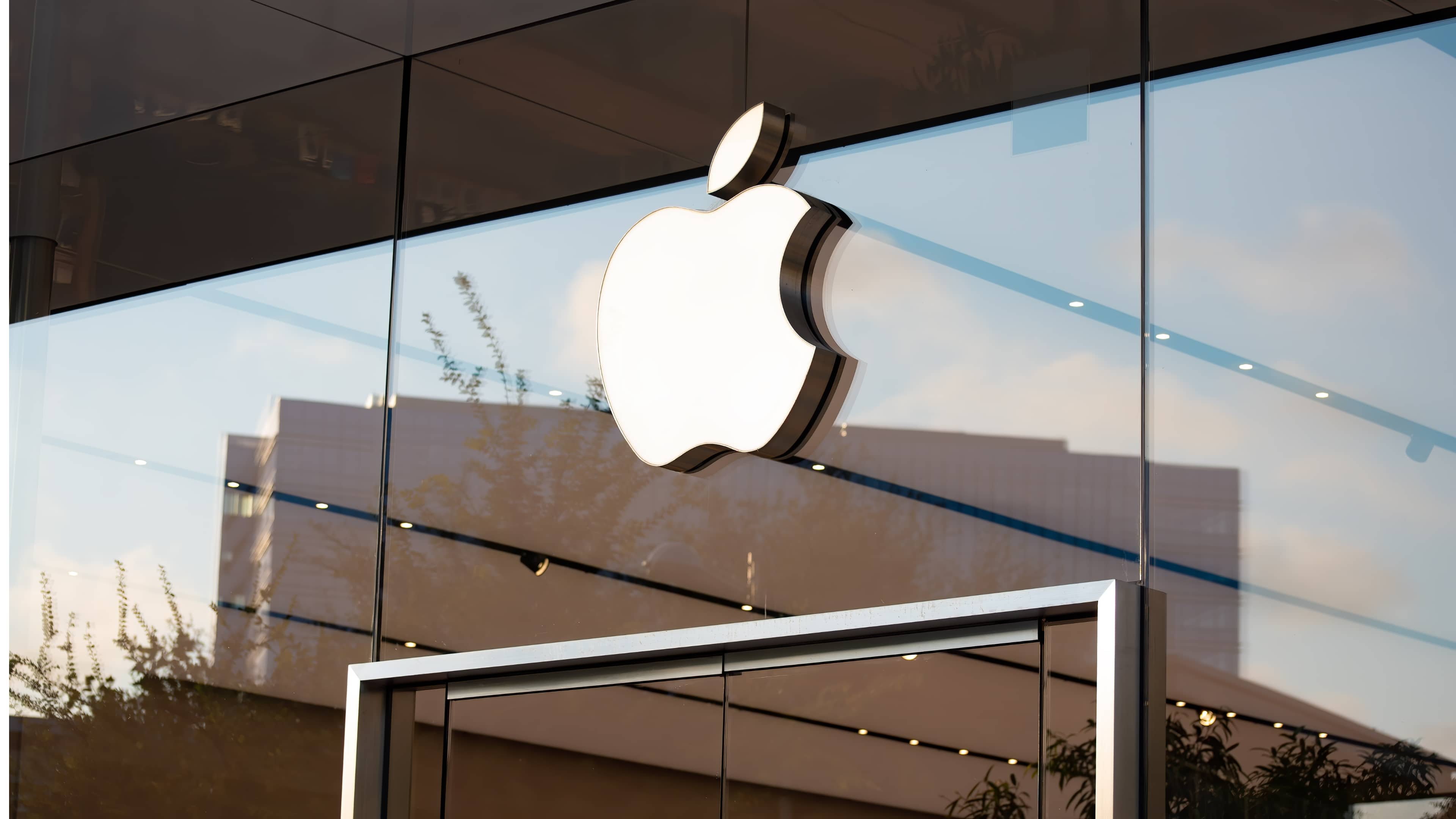 Closeup of an Apple logo above entrance to a glass Apple retail store