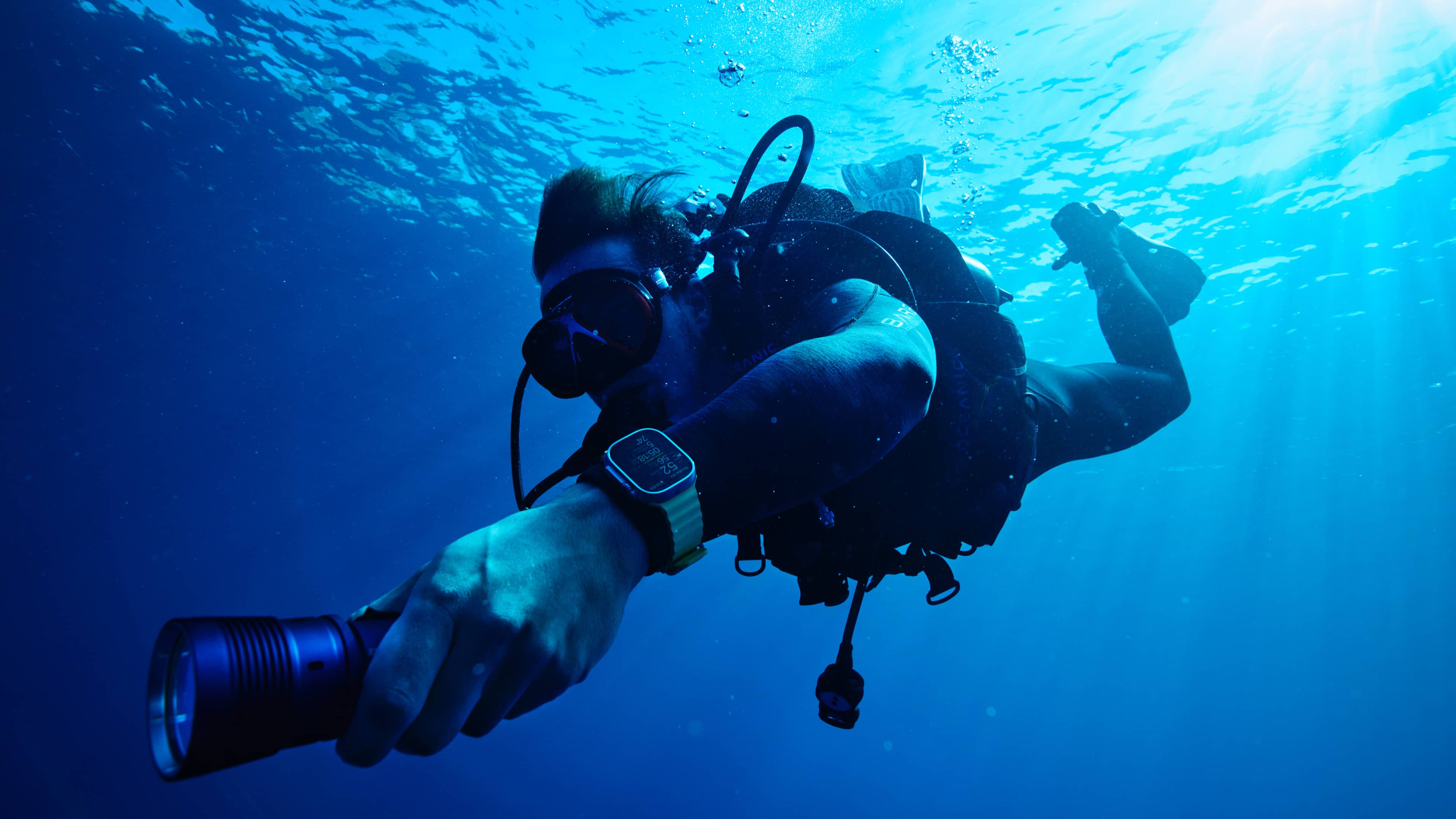 A scuba diver underwater using a flashlight and wearing Apple Watch Ultra with the Oceanic+ app providing dive computer functions 