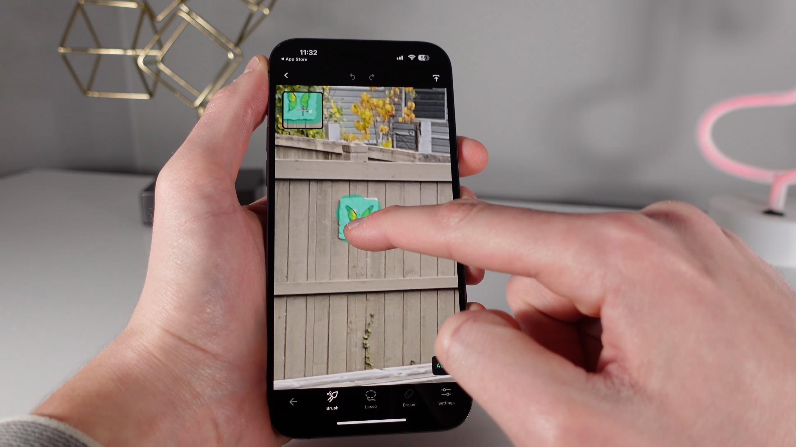 Die Hand eines Mannes manipuliert ein iPhone-Bild in der TouchRetouch-App, indem er mit seinem Finger ein Schmetterlingsschild von einem Holzzaun entfernt 