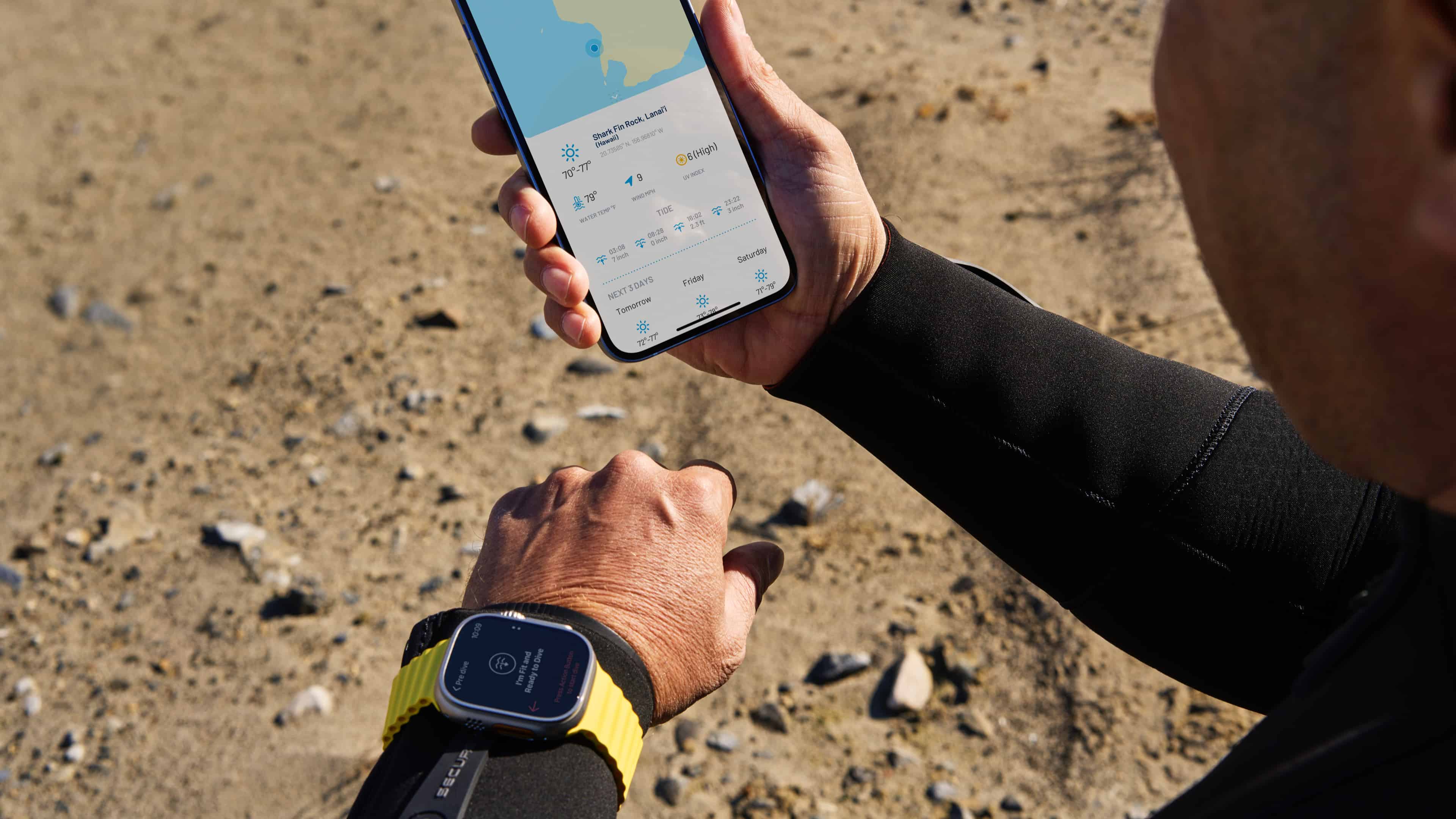 Ein Taucher am Strand, der ein iPhone in der Hand hält und eine Apple Watch Ultra trägt, führt in der Oceanic+ App eine Tauchgangsplanung durch