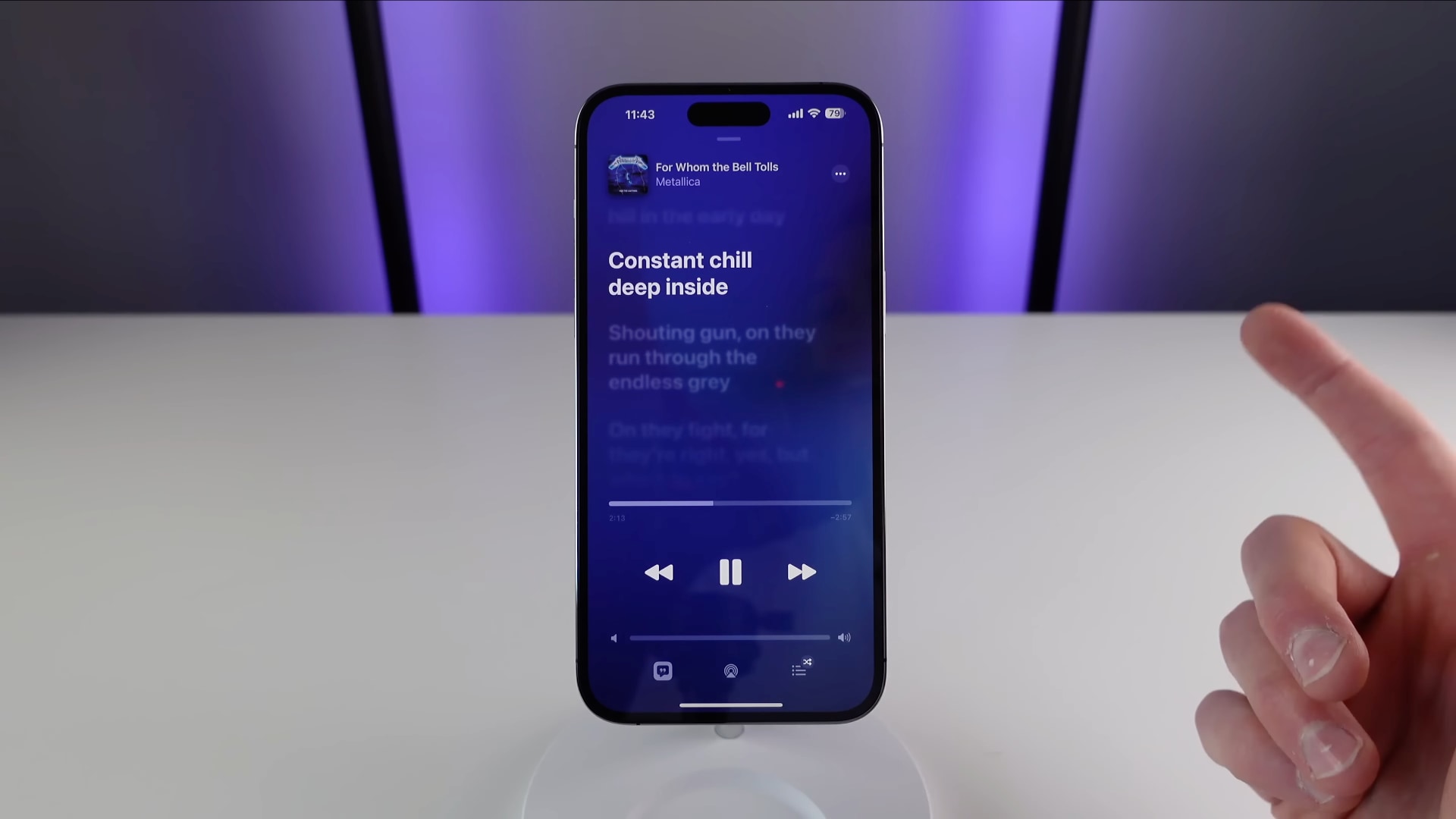 iPhone standing upright on a white table, showcasing time-synced lyrics in the Music app