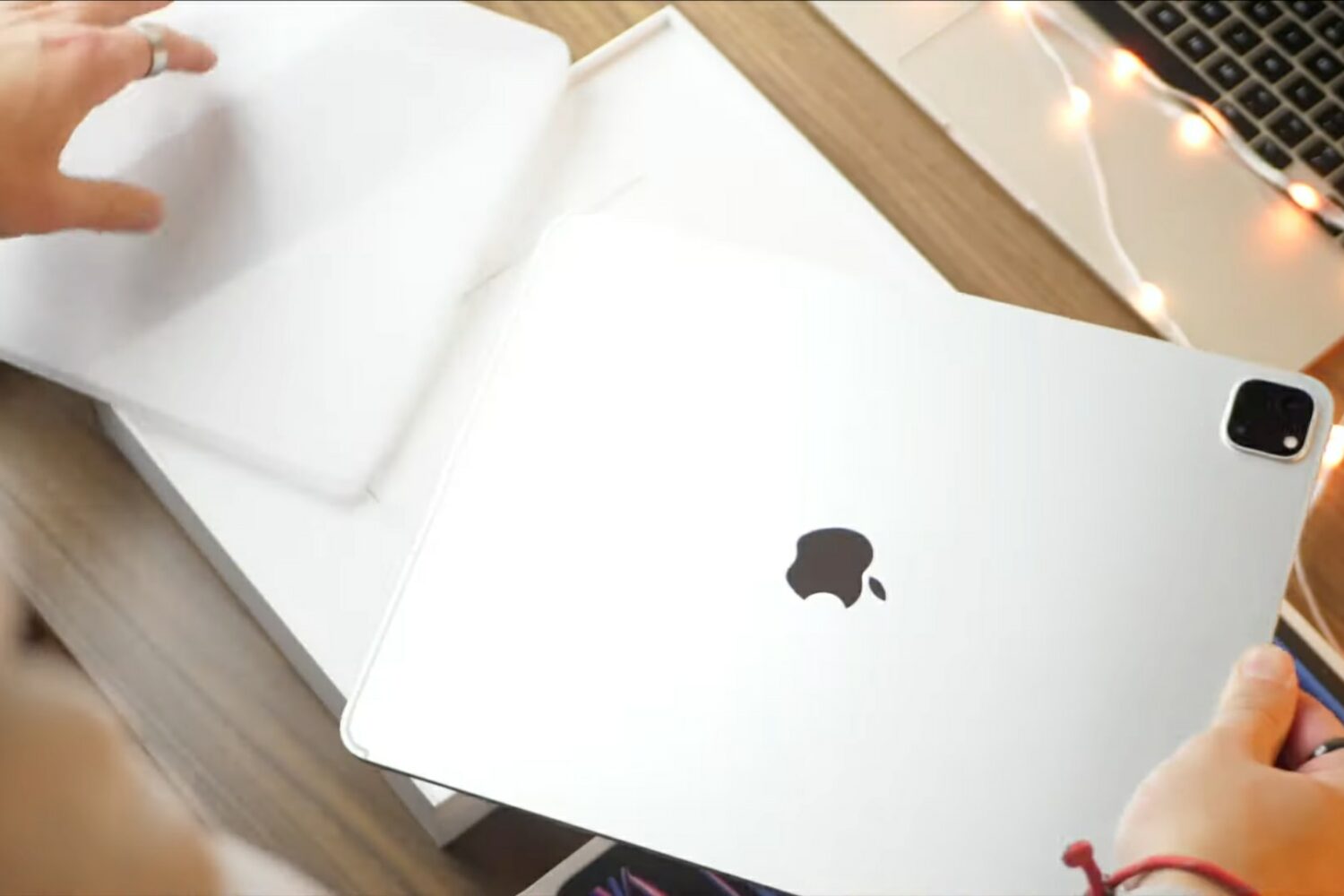 A young male's hands above a wooden desk taking the plastic wrapping off a brand new 12.9-inch iPad Pro