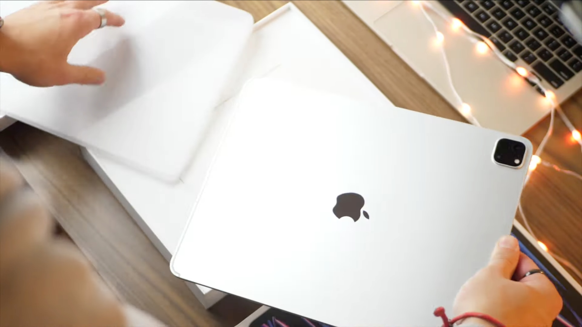 A young male's hands above a wooden desk taking the plastic wrapping off a brand new 12.9-inch iPad Pro 