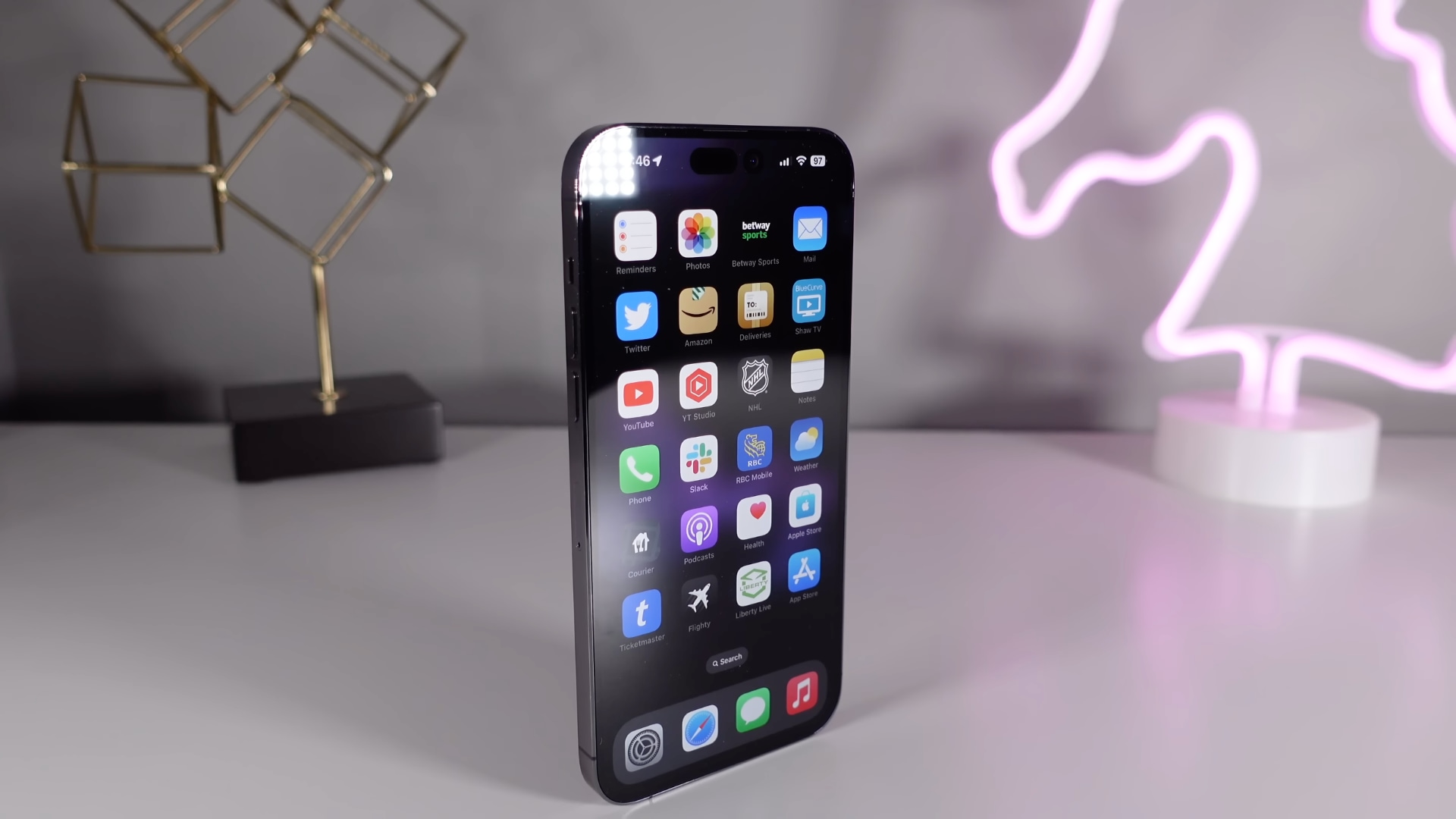 Ein tiefviolettes Apple iPhone 14 Pro aufrecht auf einem weißen Schreibtisch mit Neonstimmung im Hintergrund