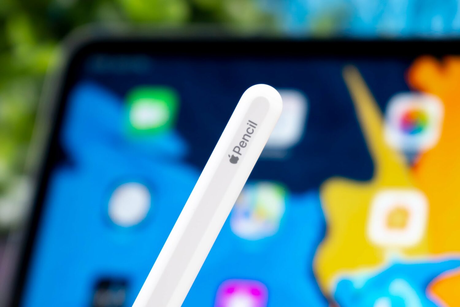 Closeup showcasing the end of Apple Pencil with branding, with a blurred iPad Pro in the background