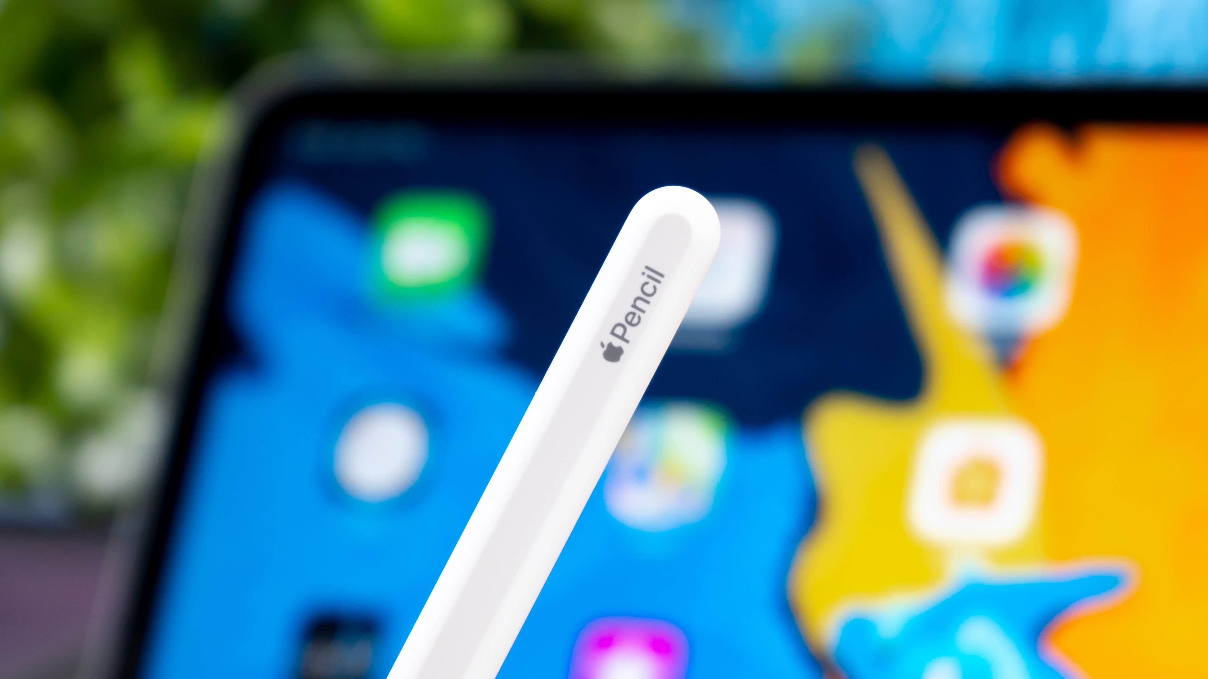 Closeup showcasing the end of Apple Pencil with branding, with a blurred iPad Pro in the background