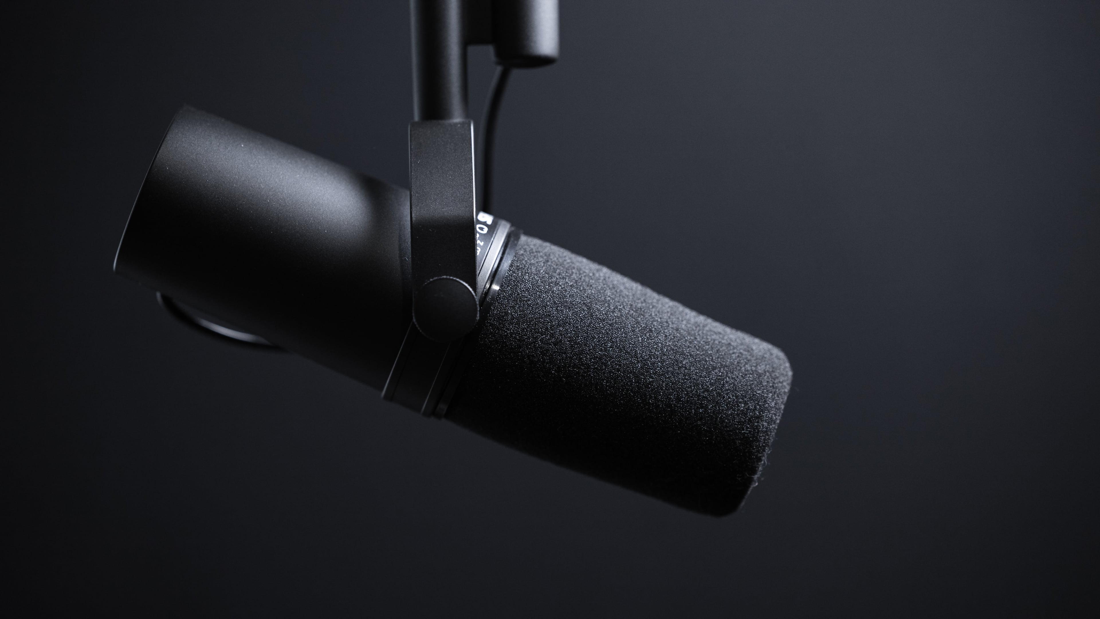 Closeup of a podcasting microphone suspended from above, set against a black gradient background 