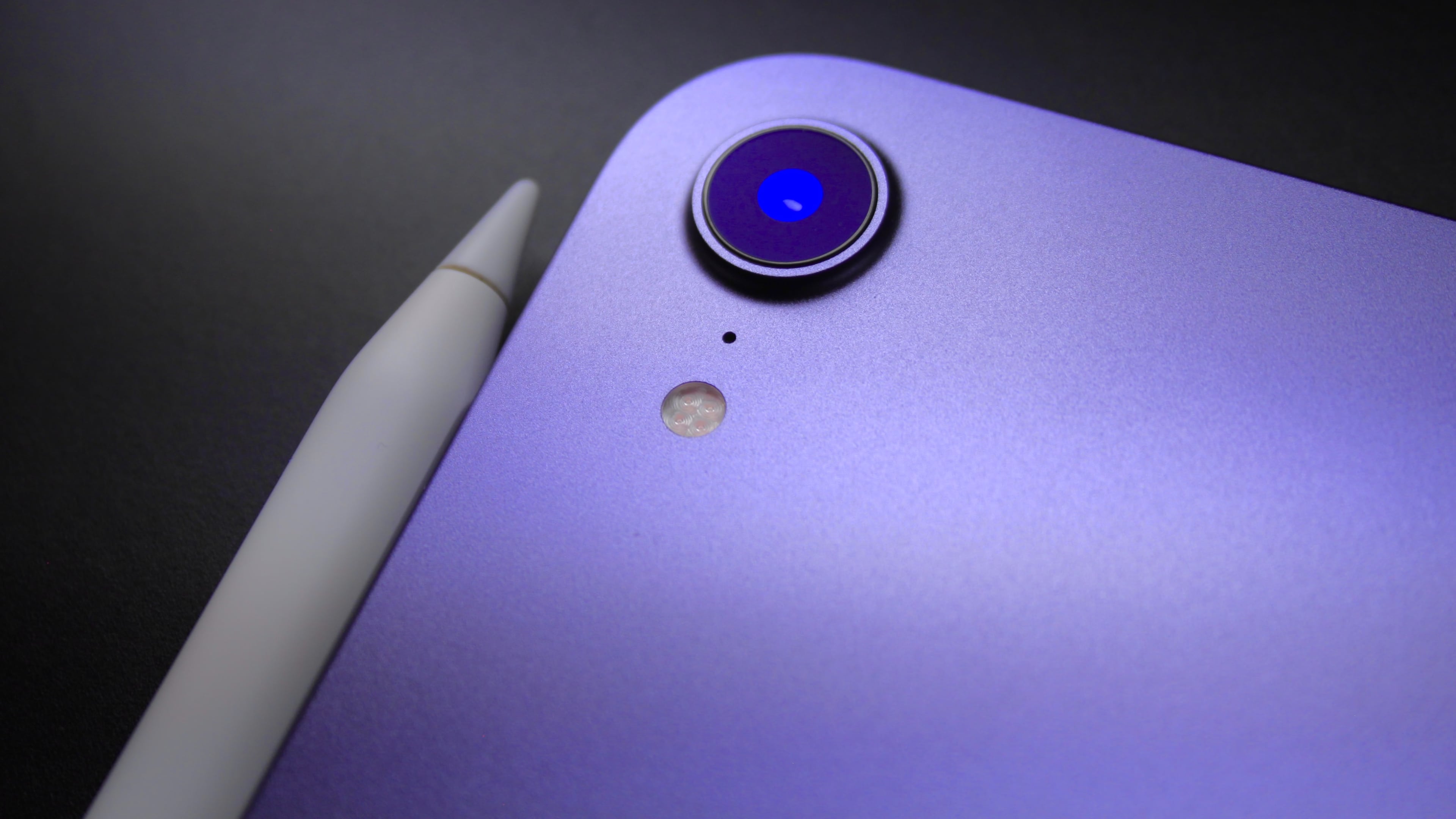 Closeup of the back camera on a purple iPad mini 6, with an Apple Pencil lying next to the tablet