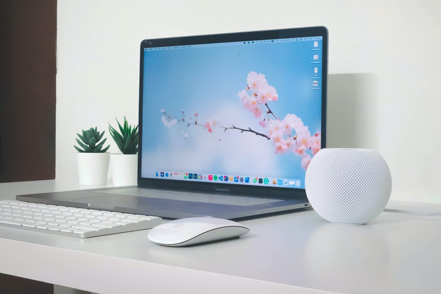 HomePod mini on a work desk next to MacBook Pro and Apple keyboard and mouse