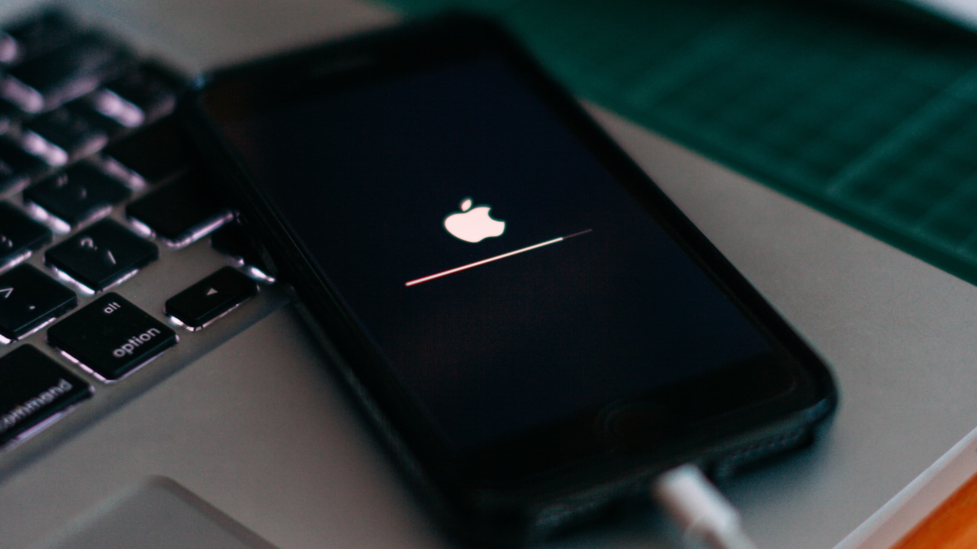 An iPhone laying on a MacBook, showing an iOS update progress bar