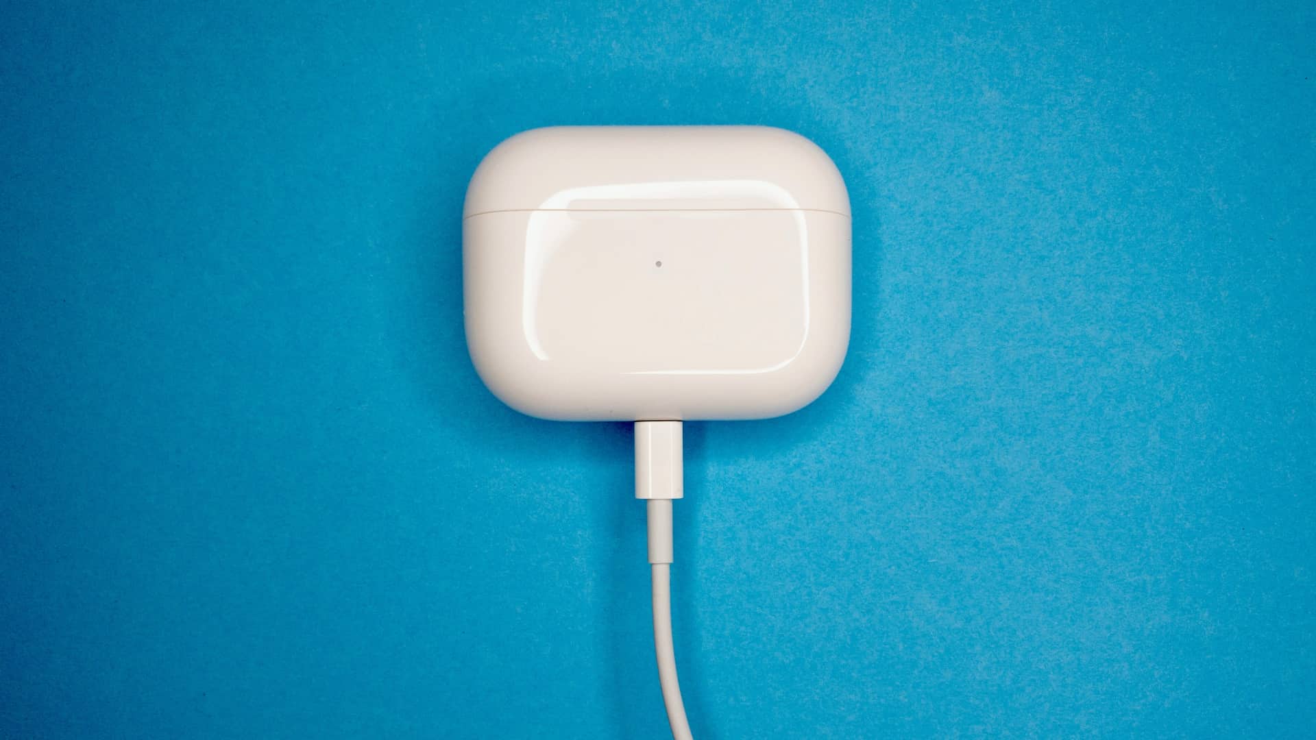 AirPods Pro in their case, charging with a Lightning to USB cable, set against a blue textured background