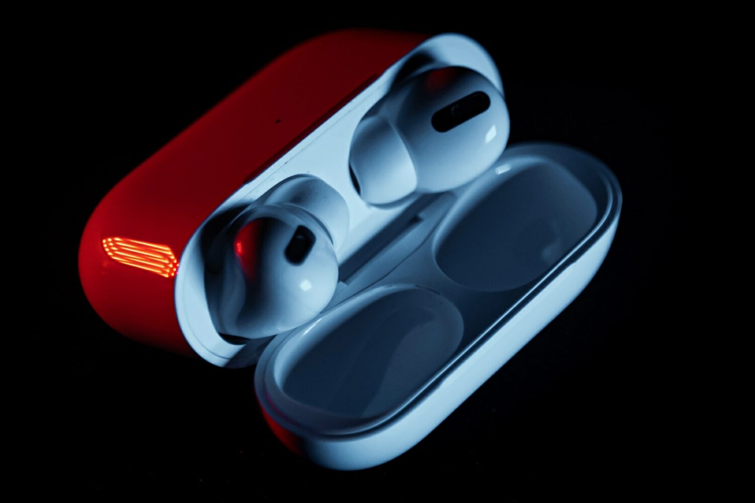 AirPods Pro in their charging case under red light, with the lid open , set against a black background