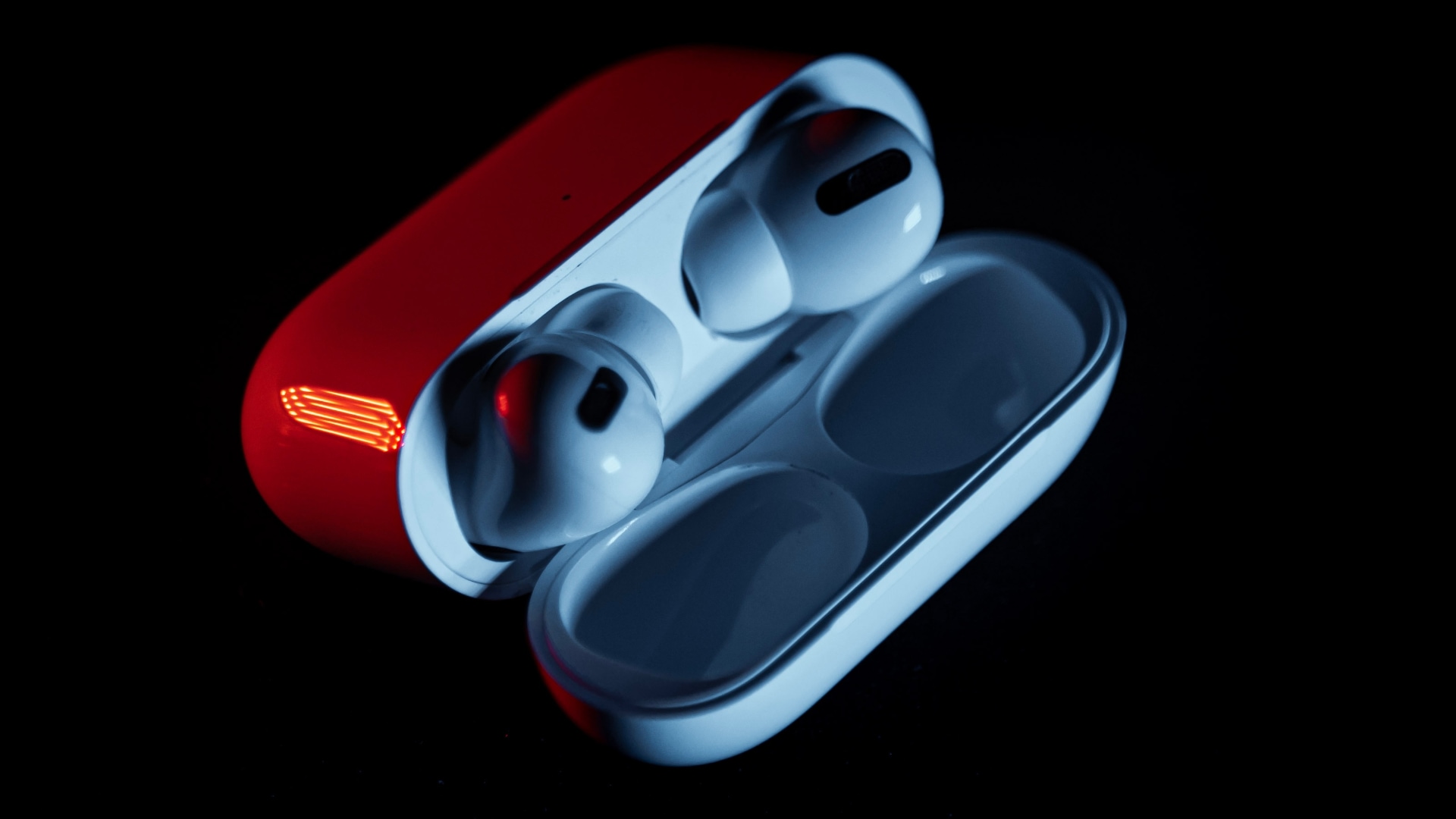 AirPods Pro in their charging case under red light, with the lid open , set against a black background