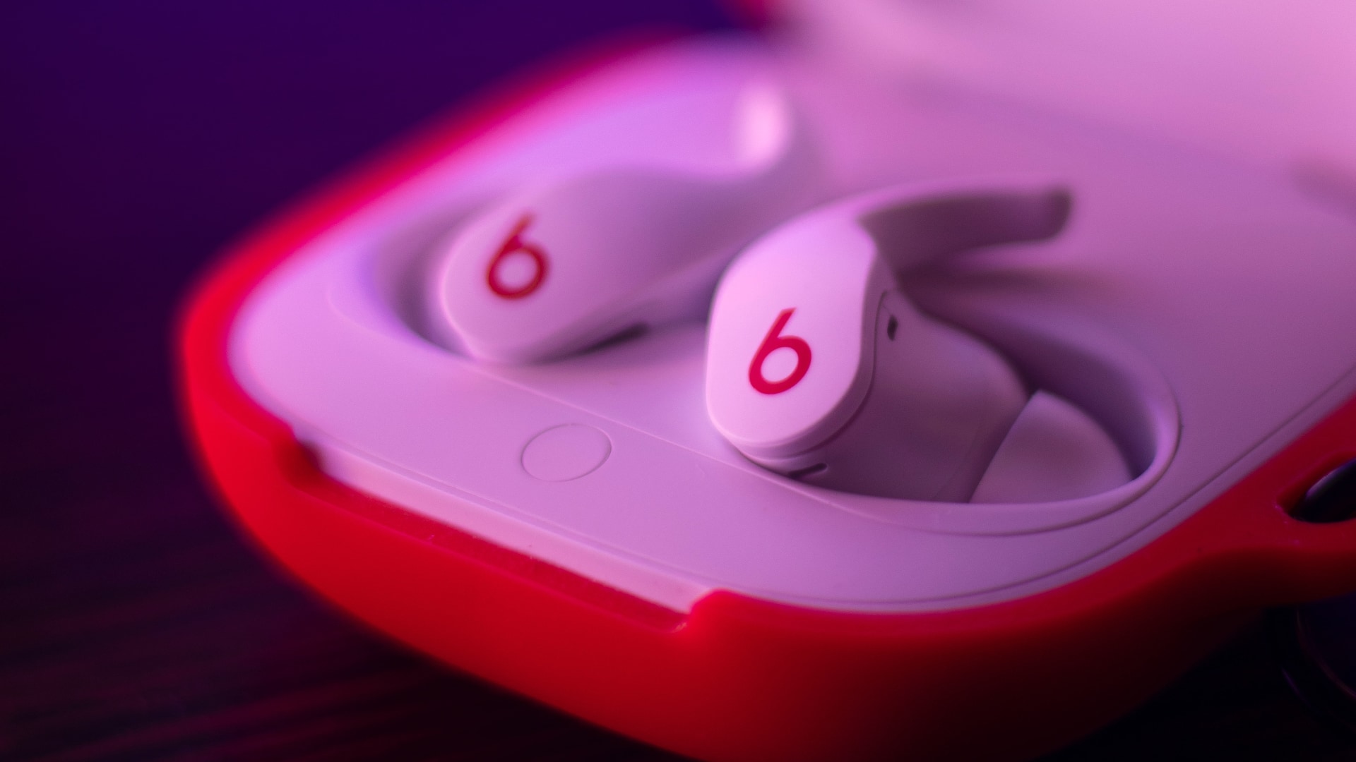 Beats Fit Pro in their charging case under red light, with the lid open