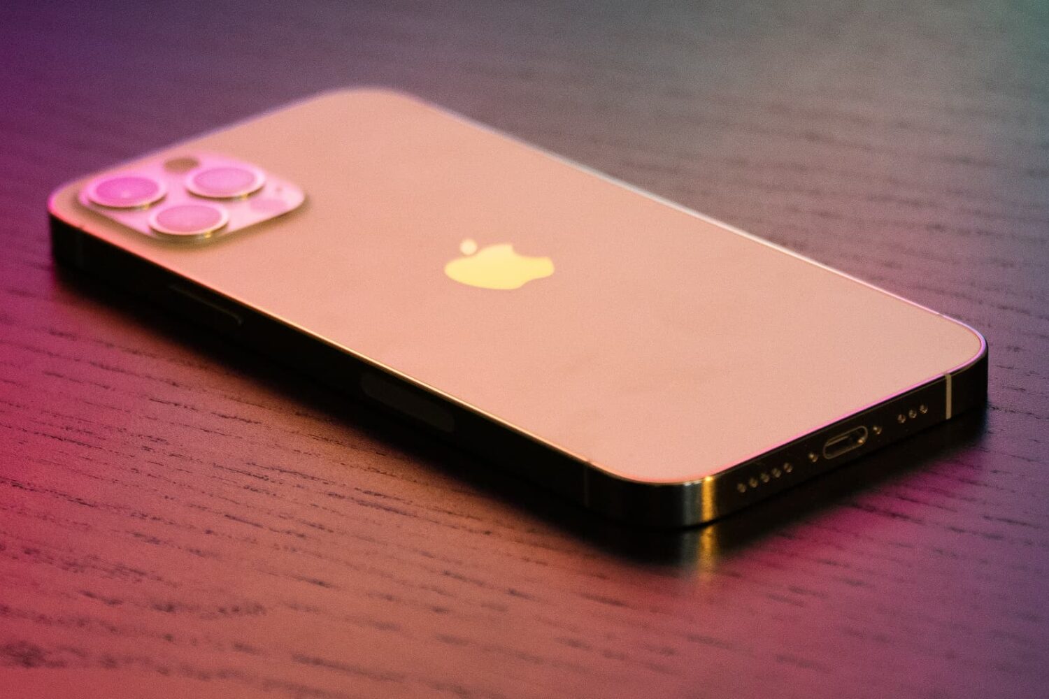 Gold iPhone 12 Pro under colorful lighting, set facedown on a wooden table