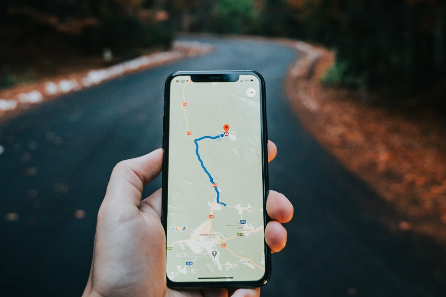 iPhone in a male's hand in the woods, displaying navigation directions in Google Maps