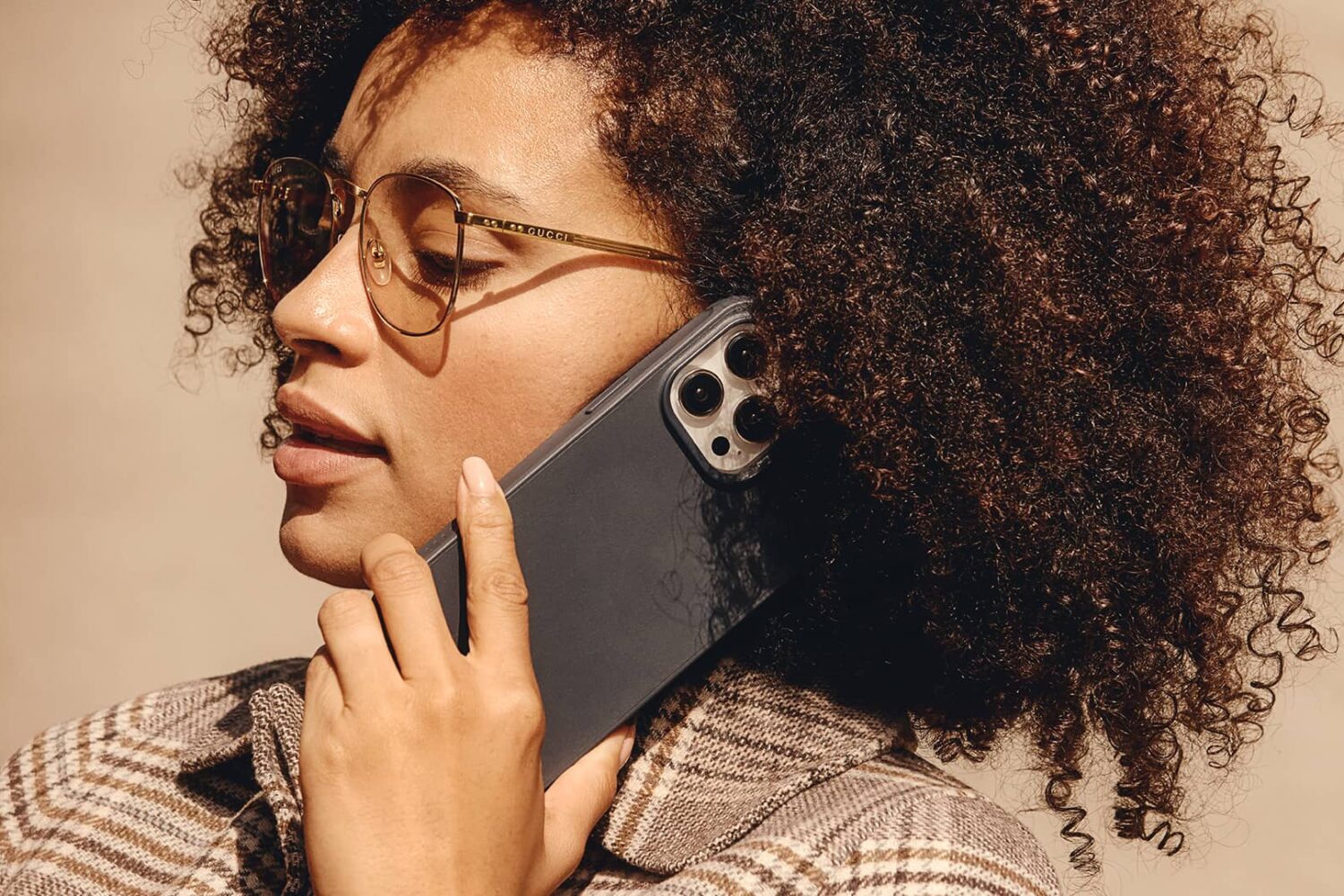 Young woman holding an iPhone 15 Pro in Mujjo's protective case against her ear