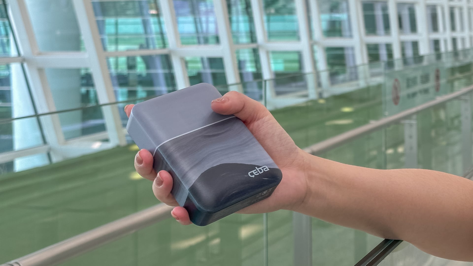 Person's hand holding Ceba RAPI power bank at the airport