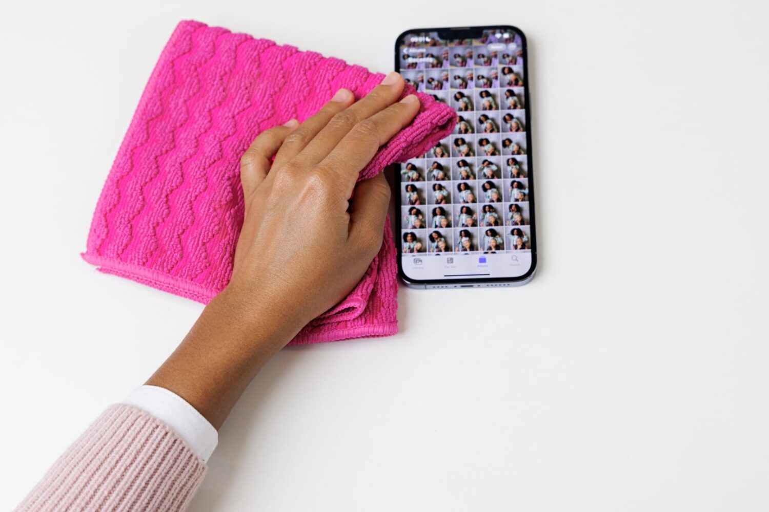 Female hand wiping an iPhone running the Photos app with a pink cleaning cloth