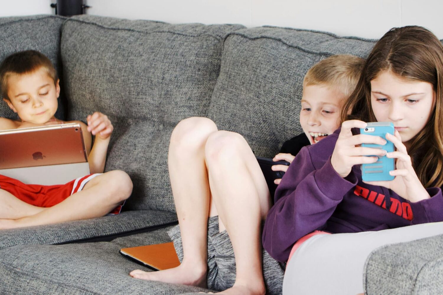 Three children sitting on a sofa and using iPhone and iPad